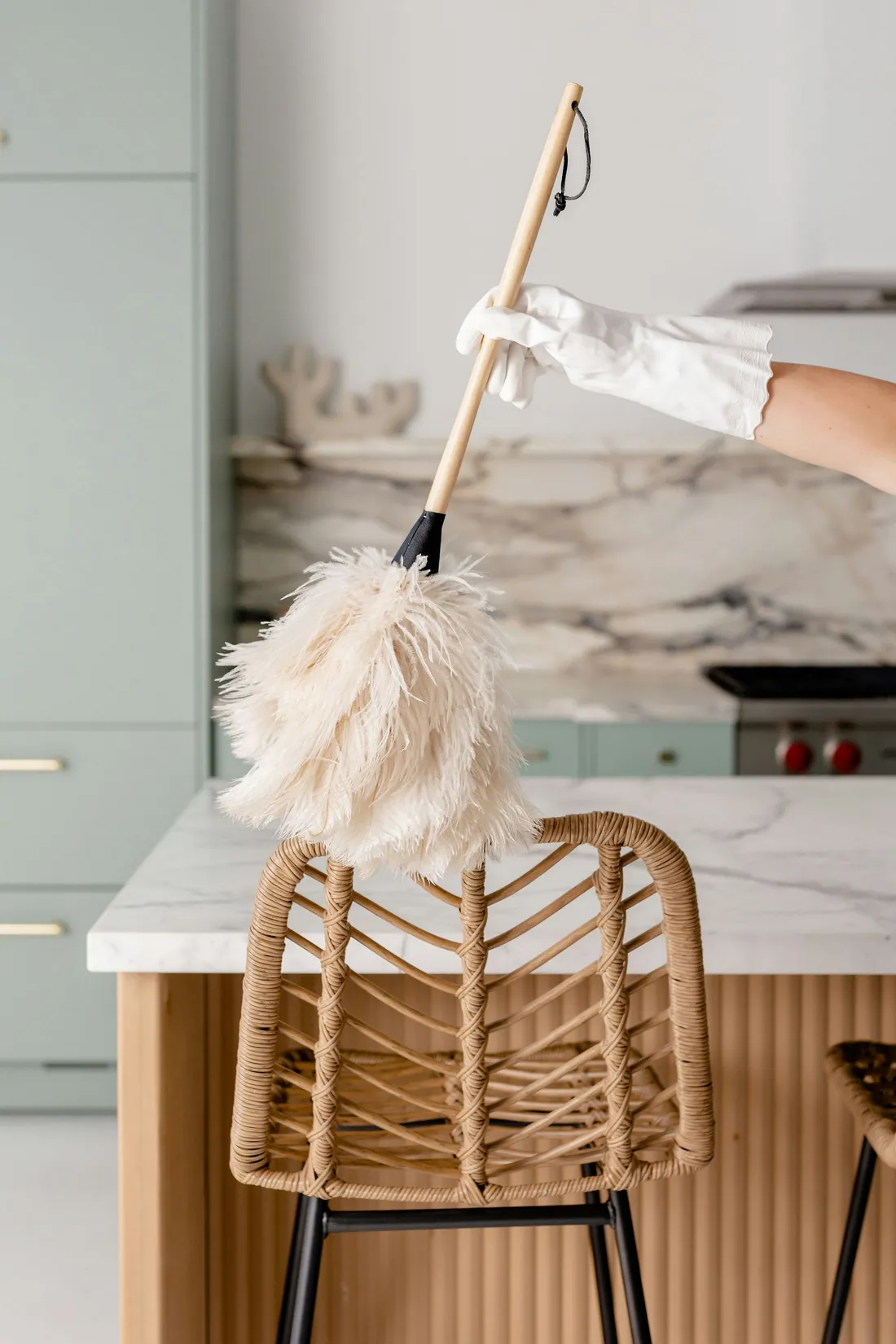 A gloved hand dusting a kitchen counter with a feather duster